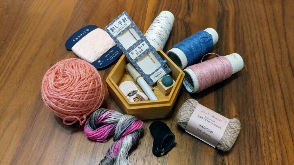 Small sewing box surrounded by various sashiko threads, embroidery floss, and yarn used for darning.